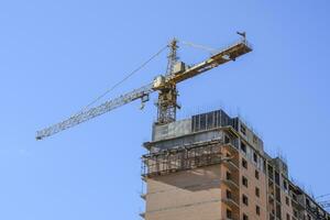 torre construção guindaste contra a azul céu e Sol. construção do uma Novo casa. construção do Novo edifícios com uma guindaste. torre guindaste foto