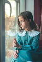 uma pensativo fofa menina senta e parece Fora a janela foto