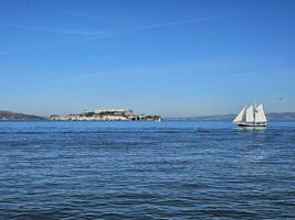 uma vela barco cruzando dentro frente do Alcatraz ilha dentro san francisco Califórnia foto
