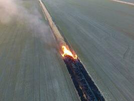 queimando seco Relva ao longo a irrigação canal. fumaça e a chama do seco grama. queimado seco grama. foto