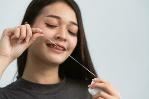 ásia mulher suspensórios usando dental fio dental. dentes suspensórios em a branco dentes do mulheres para igualar a dentes. suporte sistema dentro sorridente boca, fechar acima foto dentes, macro tomada, dentista saúde conceito.