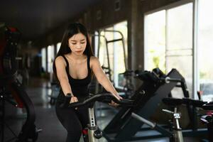 esportista asiática exercitando em uma bicicleta na academia, determinação para cardio perder peso, a torna saudável. conceito do esporte da aptidão da mulher da bicicleta de exercício. foto