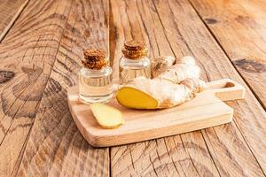 natural gengibre raiz óleo dentro dois vidro garrafas com cortiça boné em de madeira corte borda e de madeira mesa. conceito do casa cozinhando do óleo e casa corpo Cuidado foto