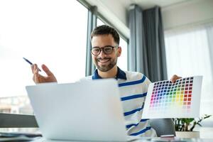 jovem cara mostrando cor amostras às computador portátil tela às casa escritório, apresentando gráfico Projeto projeto em controlo remoto reunião. milenar desenhador selecionando gama para futuro casa interior foto