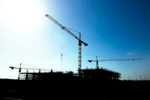 silhueta do uma construção local com torre guindastes e inacabado construção foto