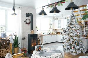 Natal decoração dentro branco cozinha com queimando fogão lareira, festivo bagunça, Vila interior com uma Nevado Natal árvore. Novo ano, Natal humor, acolhedor lar. foto