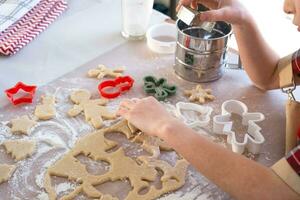 as mãos da mãe e da filha cortaram biscoitos da massa com moldes sobre um tema de natal na forma de um boneco de neve, uma árvore de natal, estrelas foto