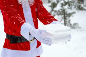 recipientes de serviço de entrega de comida nas mãos do papai noel ao ar livre na neve. promoção de véspera de natal. pedido quente pronto, caixa plástica descartável. catering de férias de ano novo. copie o espaço, simular foto