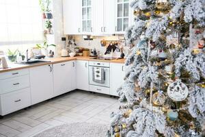 Natal decoração dentro branco cozinha, festivo bagunça, Vila interior com uma Nevado Natal árvore e fada luzes. Novo ano, Natal humor, acolhedor lar. foto