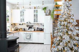 festivo Natal decoração dentro branco cozinha, moderno rústico interior com uma Nevado Natal árvore e fada luzes. Novo ano, Natal humor, acolhedor lar. a geral plano foto