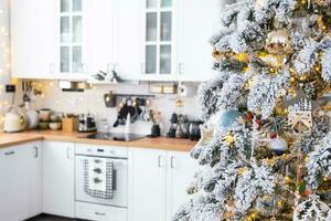 festivo Natal decoração dentro branco cozinha, moderno rústico interior com uma Nevado Natal árvore e fada luzes. Novo ano, Natal humor, acolhedor lar. a geral plano foto