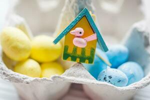 uma grupo do amarelo e azul ovos dentro ovo caixa. perto a casa com uma pássaro. a conceito do a abandonado casa do Ucrânia para a Páscoa feriado. foto