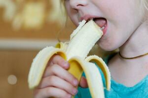 retrato do uma pequeno menina comendo uma banana. a conceito do saudável Comida. uma fresco rápido lanche foto