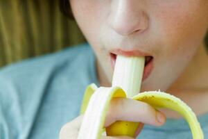 retrato do uma Adolescência Garoto comendo uma banana. foto do uma pessoal boca e lábios com uma banana. fresco fruta. saudável alimentos para crianças