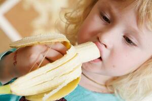 retrato do uma pequeno menina comendo uma banana. a conceito do saudável Comida. uma fresco rápido lanche foto
