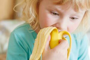 retrato do uma pequeno menina comendo uma banana. a conceito do saudável Comida. uma fresco rápido lanche foto