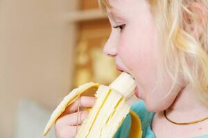 retrato do uma pequeno menina comendo uma banana. a conceito do saudável Comida. uma fresco rápido lanche foto