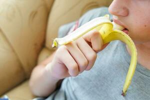 retrato do uma Adolescência Garoto comendo uma banana. foto do uma pessoal boca e lábios com uma banana. fresco fruta. saudável alimentos para crianças