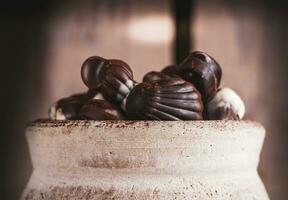 Concha em forma chocolates com creme dentro uma argila jarra foto