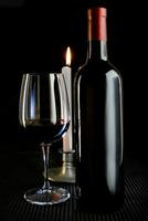 estúdio composição com vermelho vinho garrafa e vidro e queimando vela foto