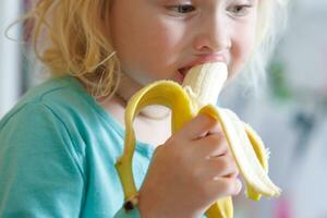 retrato do uma pequeno menina comendo uma banana. a conceito do saudável Comida. uma fresco rápido lanche foto