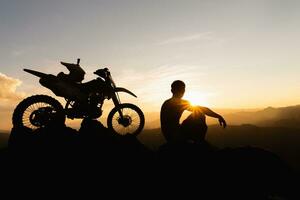 homem com motocross bicicleta contra lindo luzes, silhueta do uma homem com motocross motocicleta em topo do Rocha Alto montanha às lindo pôr do sol, enduro motocicleta viagem conceito. foto