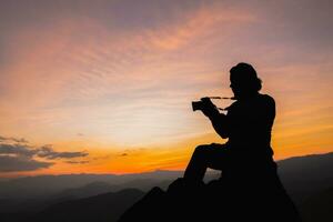 silhueta do uma fotógrafo em topo do uma montanha às pôr do sol foto