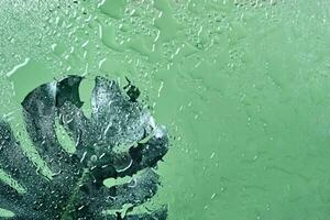 verde molhado fundo com água gotas em vidro e monstera folha através vidro. verde água textura fundo foto