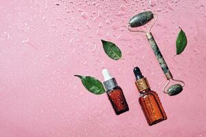 orgânico cosméticos, verde folhas e jade massagem rolo. cuidados com a pele produtos garrafa e água gotas em Rosa fundo foto