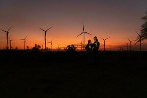 engenheiros trabalhando em vento turbinas Fazenda às pôr do sol, vento turbinas estão alternativo energia fonte. foto