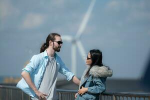 jovem casal relaxante de a vento turbina em a lago foto