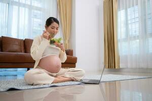 grávida mulher come salada Como uma lanche enquanto sentado em a chão do dela lar. foto