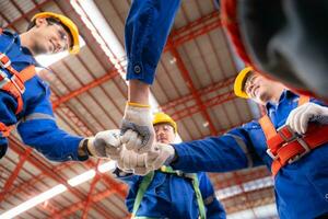 debaixo Visão do uma equipe do industrial trabalhadores em pé juntos dentro uma armazém, foco em punho colisão mãos juntos foto