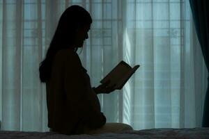 dentro silhueta, grávida mulher lendo uma histórias para dela por nascer criança dentro a vivo quarto às casa foto