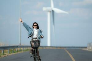 jovem mulher equitação uma bicicleta em uma estrada dentro uma moinho de vento. foto