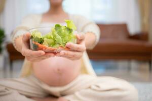 grávida mulher comendo fresco vegetal salada às lar. gravidez conceito foto