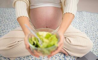 grávida mulher comendo fresco vegetal salada às lar. gravidez conceito foto
