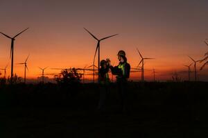 engenheiros trabalhando em vento turbinas Fazenda às pôr do sol, vento turbinas estão alternativo energia fonte. foto