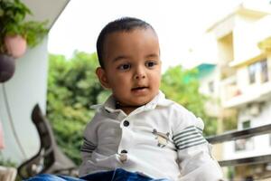 bebê Garoto às casa sacada. brilhante retrato do feliz criança sentado em a mesa. pequeno 1 ano velho Garoto durante a dia luz às casa sacada. foto