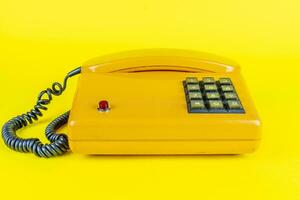 amarelo plástico vintage Telefone com vermelho botão em uma amarelo fundo foto