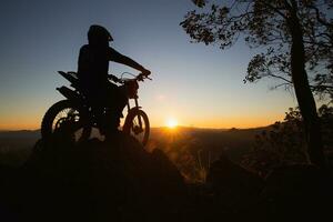 homem com motocross bicicleta contra lindo luzes, silhueta do uma homem com motocross motocicleta em topo do Rocha Alto montanha às lindo pôr do sol, enduro motocicleta viagem conceito. foto