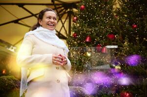 sorridente mulher às parque de diversões, olhando ausente, em pé contra uma Natal árvore decorado com guirlandas. bokeh em primeiro plano foto