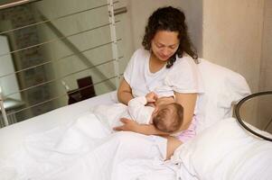 confiante jovem mulher mãe goza dela maternidade sair estilo de vida, amamenta dela bebê enquanto acorda acima dentro a manhã foto