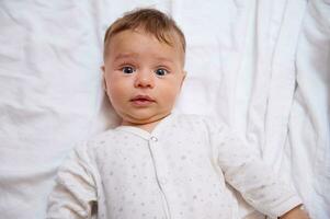 fechar-se retrato do fofa bebê Garoto 4-6 meses velho olhando às Câmera, deitado em branco cama folhas em a cama. cópia de de Anúncios espaço foto