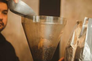 ásia homem barista preparação derramando café feijão para dentro moer café dentro café fazer compras. foto