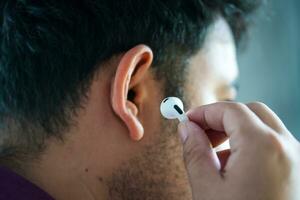 Bangkok, Tailândia - dezembro 24, 2023 empresário segurando airpods 3 sem fio Bluetooth no ouvido fone de ouvido inserindo dele orelha foto