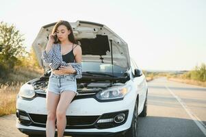 jovem sexy mulher com quebrado carro chamando em a célula telefone. foto