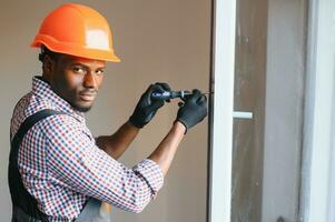 bonito jovem africano americano homem instalando baía janela dentro Novo casa construção local foto