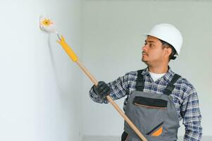 a indiano apartamento reparar trabalhador tintas uma branco parede com uma rolo. foto