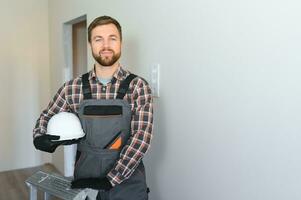 retrato do uma confiante reparador com barba em pé dentro esvaziar apartamento foto